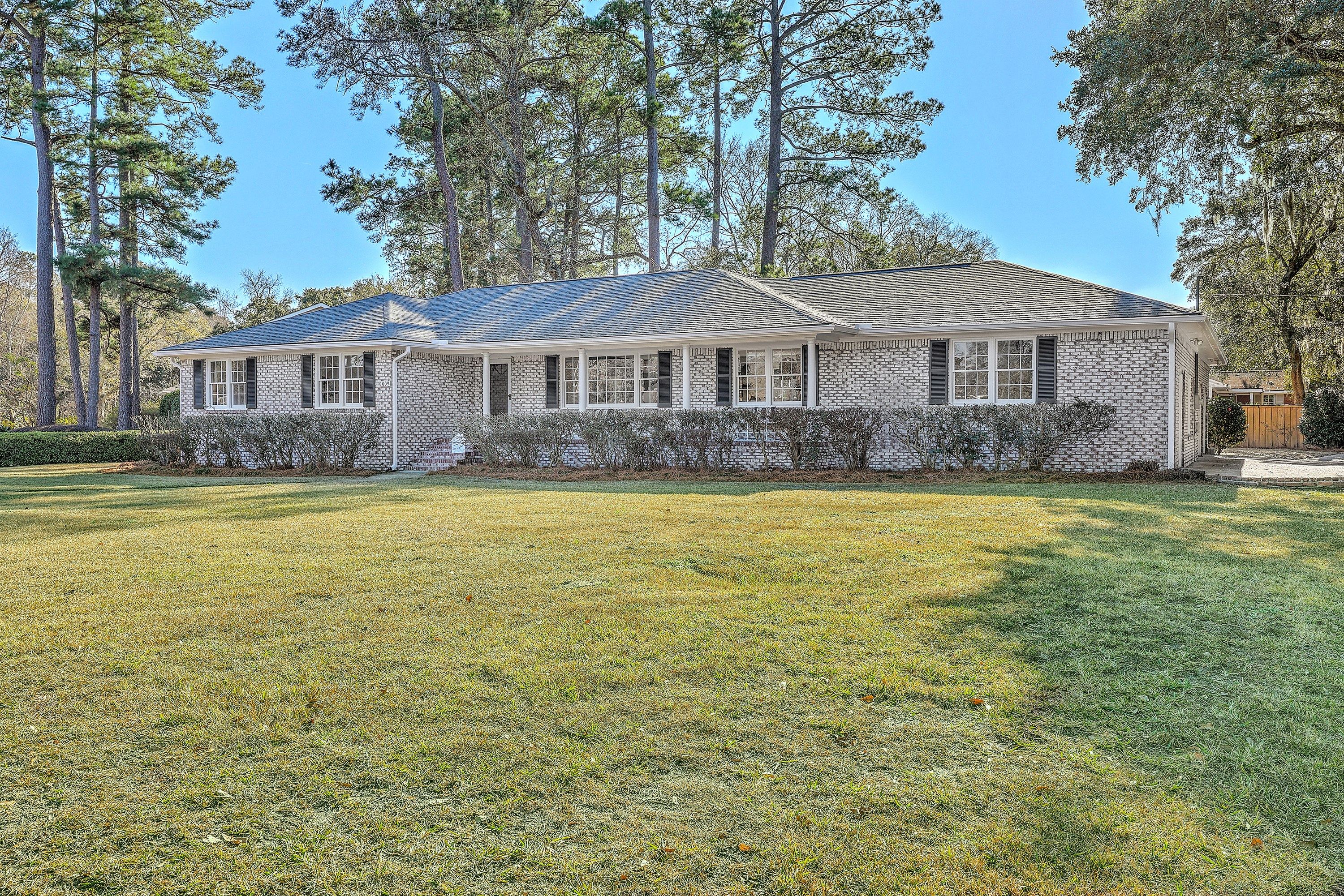 1009 Southgate Drive after renovation: painted brick ranch with black shutters on a large lawn under tall pines