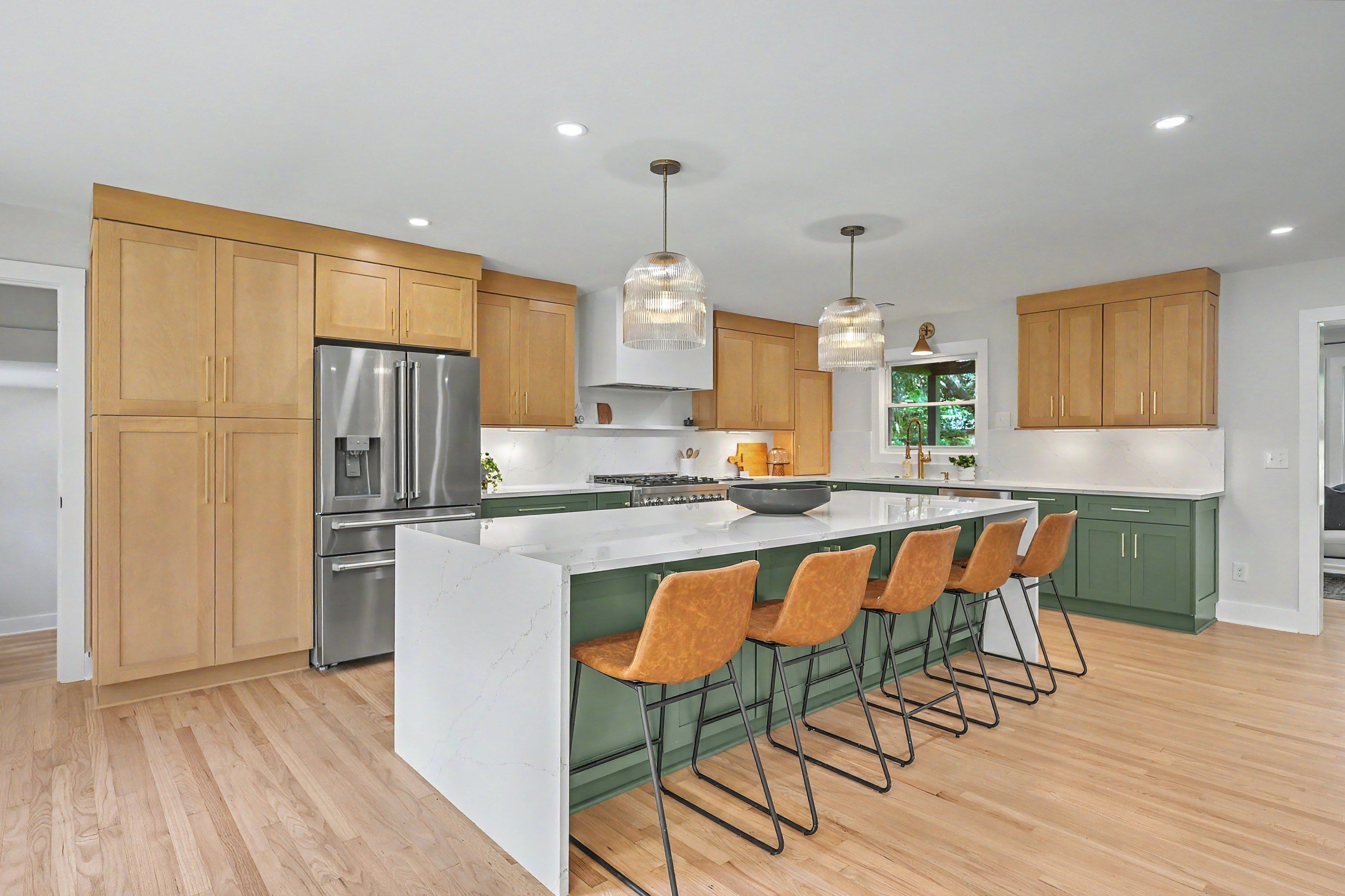 Renovated kitchen with natural wood and green cabinetry, waterfall island and brass pendants