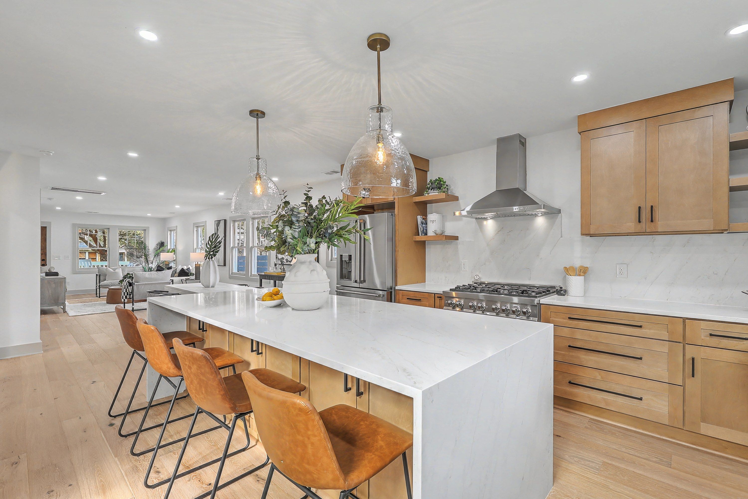 Kitchen with a waterfall quartz island, natural wood cabinetry and a 36-inch gas range, open to the living room